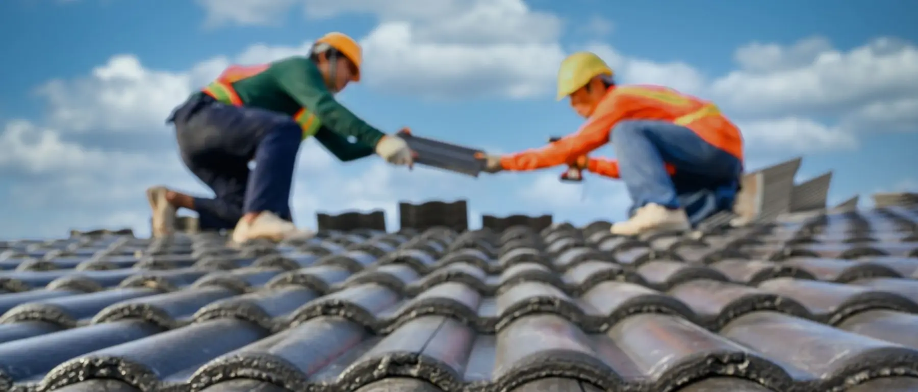 A roofing crew in bright pink shirts installs tiles on a sloped roof.