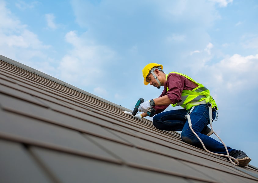 A contractor in safety gear performs a detailed roof repair.