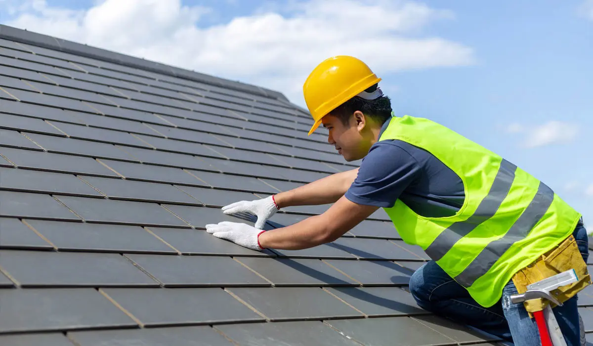 A worker in a yellow hard hat installs tiles on a roof.